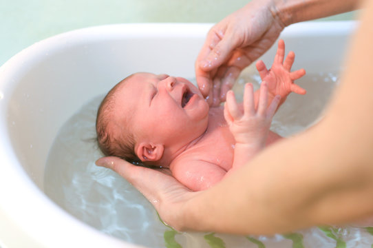 Crying newborn baby girl bathing
