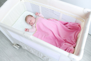 Lovely newborn girl sleeps in travel crib
