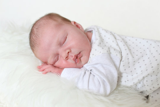 3-weeks newborn girl sleeps on fur white plaid