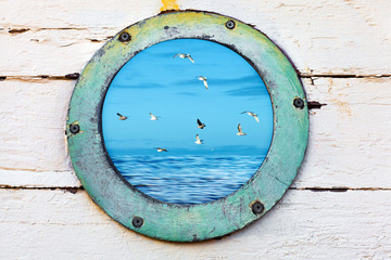 Vintage old porthole window looks out at birds and sea