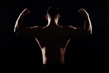 Fototapeta na wymiar Back of athletic man showing muscles on black background