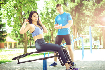 Woman doing sit ups outdoor with her trainer.