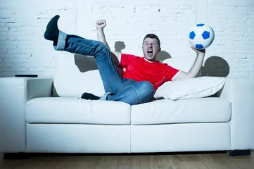 Gordijnen crazy fanatic  man as football fan watching game on television wearing red team jersey celebrating goal © Wordley Calvo Stock