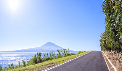 Fototapeta na wymiar asphalted road in Azores runs along the grassy shores of the Atlantic Ocean, on a background of of an extinct volcano and the blue sky