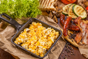 English breakfast with scrambled eggs, sausages, bacon, vegetable and spices
