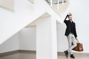 Young man with bag looking away under stairway