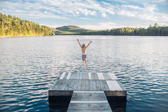 Young boy jumping off jetty into lake, rear view