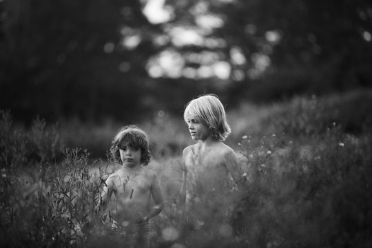 Two boys walking in field with long grass, black and white