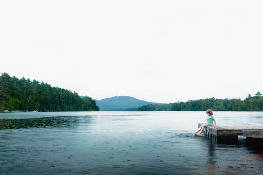Young boy sitting on jetty, dipping feet in water
