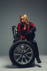 Obraz na płótnie Canvas Female in motorcycle uniform posing with car wheel.