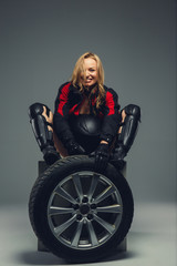 Fototapeta na wymiar Female in motorcycle uniform posing with car wheel.