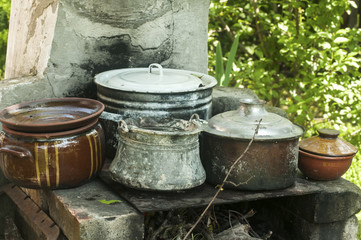 Outdoor fireplace in rural yard with stacks of old metal pots and clay cookware
