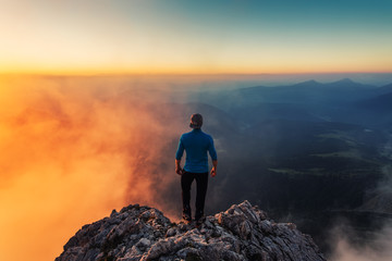 Rear view of man on top of cloudy rocky mountain in sunlight