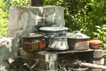 Outdoor fireplace in rural yard with stacks of old metal pots and clay cookware