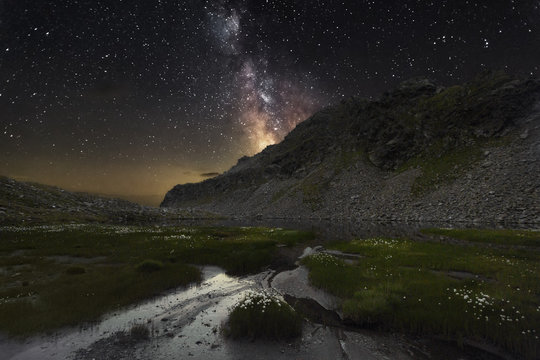waterhole by rocky mountains under starry sky