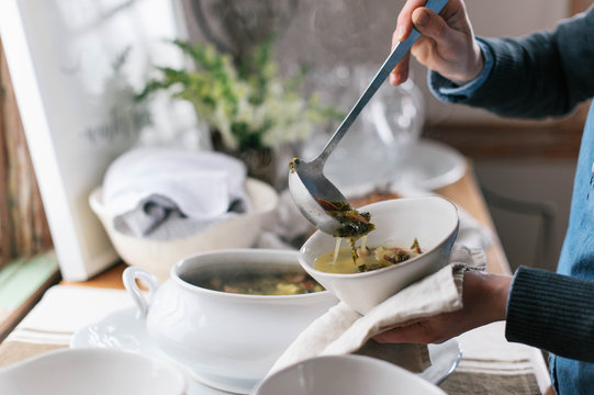 Hands of person serving soup in a bowl with ladle
