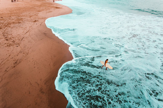 Surfer walking into ocean carrying sufboard