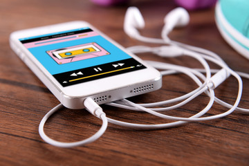 White smart phone with headphones on wooden background