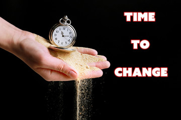 Silver pocket clock in hands and sand flowing away on black background