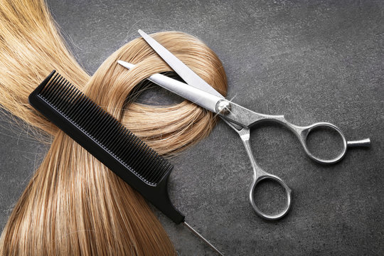 Fototapeta Nożyczki fryzjerskie z grzebieniem i pasmem blond włosów na szarym tle