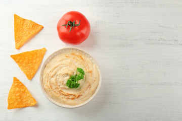 Ceramic bowl of tasty hummus with chips and parsley on table