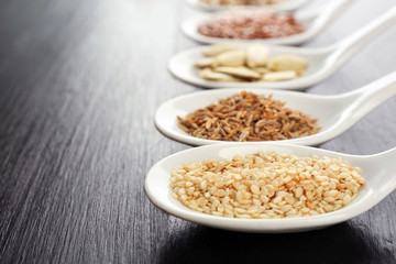 Different kinds of seeds in spoons on wooden table