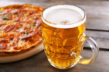 Tasty pizza and glass of beer are on wooden table, close up