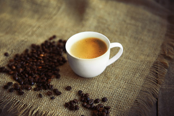 Cup of coffee with beans on sackcloth background