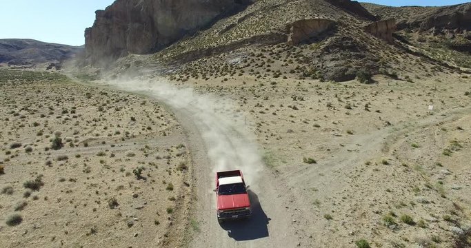Aerial scene of car traveling on dirt road, dry, rocky, landscape. Monumental scenery. Car leves dust while driving. Starts near car ends far, high. Canyon of Piedra Parada, Patagonia Argentina. 