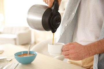 Young man pouring coffee into cup in kitchen