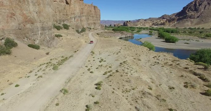 Aerial scene of car traveling in dirt road between rocky dry cliffs and alluvial river. Monumental place. Canyon of Piedra parada, Patagonia, Argentina. Desertic, rocky scenery. 