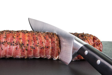 Gegrilltes Schweinefilet im Speckmantel und Pfefferkruste wird mit Fleischmesser geschnitten. - 112684422