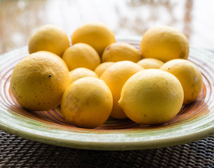 Natural looking lemons on coloured plate on rattan table with window reflection in background (selective focus and cropped)