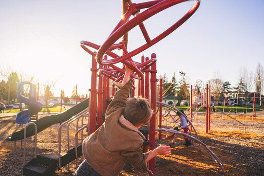 Rear view of boy swinging on monkey bars in playground