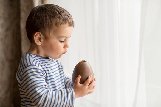 Boy standing by window eating a large chocolate easter egg