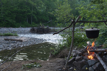 Black pot on a background of trees and river. Over the fire.