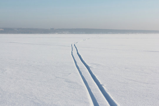 Two ski tracks leaving afar on a snow field at sunset