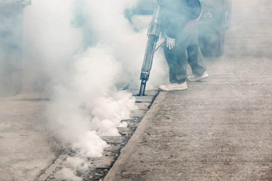 Worker fogging street drain with insecticides to kill aedes mosquito