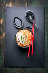 Asian noodles with vegetables and mushrooms, soy sauce, sticks on a dark background, top view with copy space 