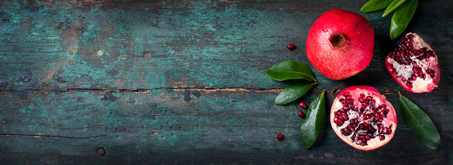 Fresh juicy pomegranate - whole and cut, with leaves on a wooden vintage background, top view,...