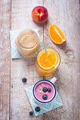 Fototapeta na wymiar A mix of three smoothies with blueberry, orange and peach on a wooden background, top view