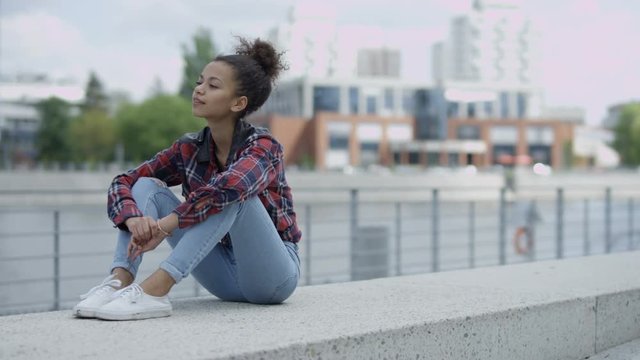 Beautiful smiling african woman in urban background. Fashion young african woman relaxing in a city, wearing a red checkered shirt and blue jeans.