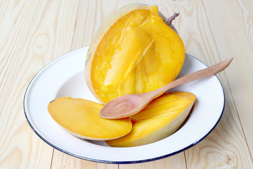 Delicious ripe mango fruit with wood spoon in whiter dish on wood background.