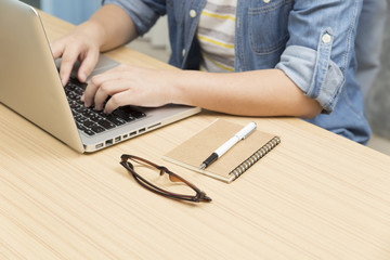 woman using laptop computer with eyeglasses, notebook and pen