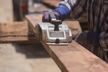 worker planing a wood with a electric plane