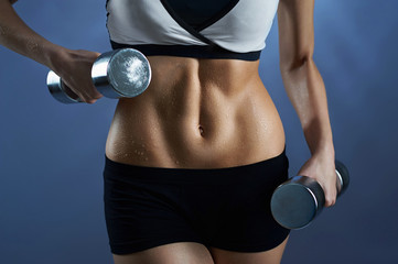 Fototapeta na wymiar Sweating hard. Cropped shot of a female wearing workout gear holding weights near her toned sweaty abs
