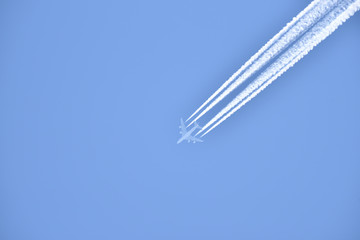 White airliner transports passengers while it pulling white contrails in blue sky