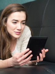 Girl reading e book on the sofa at home.