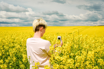 Fototapeta premium A beautiful young woman on a field. Stylish blond girl with red lips standing in the yellow field on a sunny day. Concept of freedom and happiness. Traveling having fun. 
