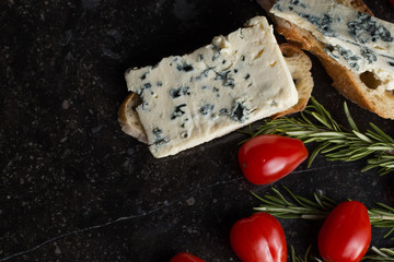 Blue cheese with french baguette, tomato and herbs on black marble table. Traditional snacks in France and Italy.